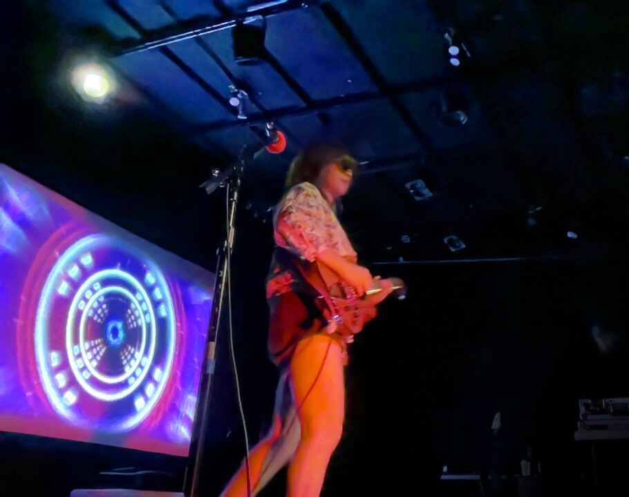 ANI with a guitar on stage and a video screen with cool graphics on it behind her